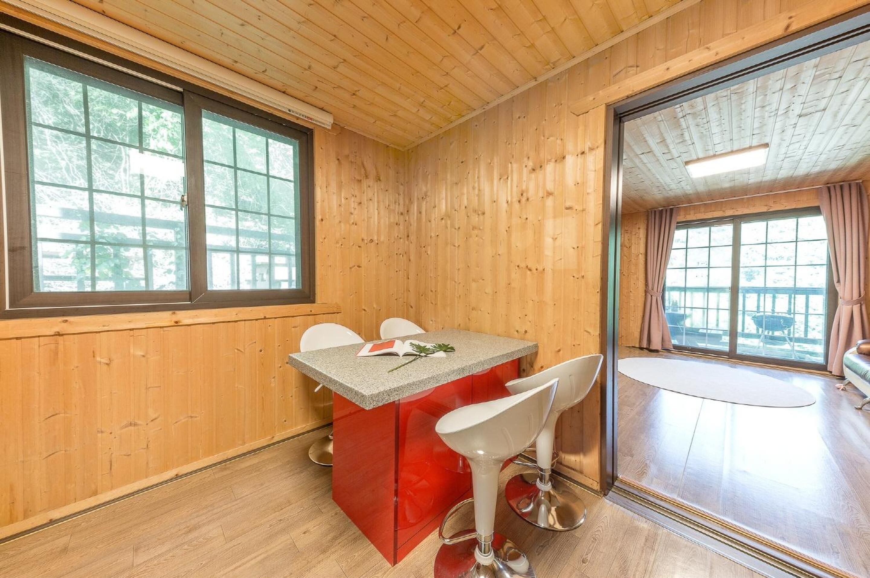 A wooden interior with a red island bar, white bar stools, and large windows.