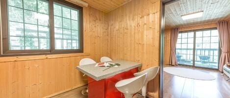 A wooden interior with a red island bar, white bar stools, and large windows.