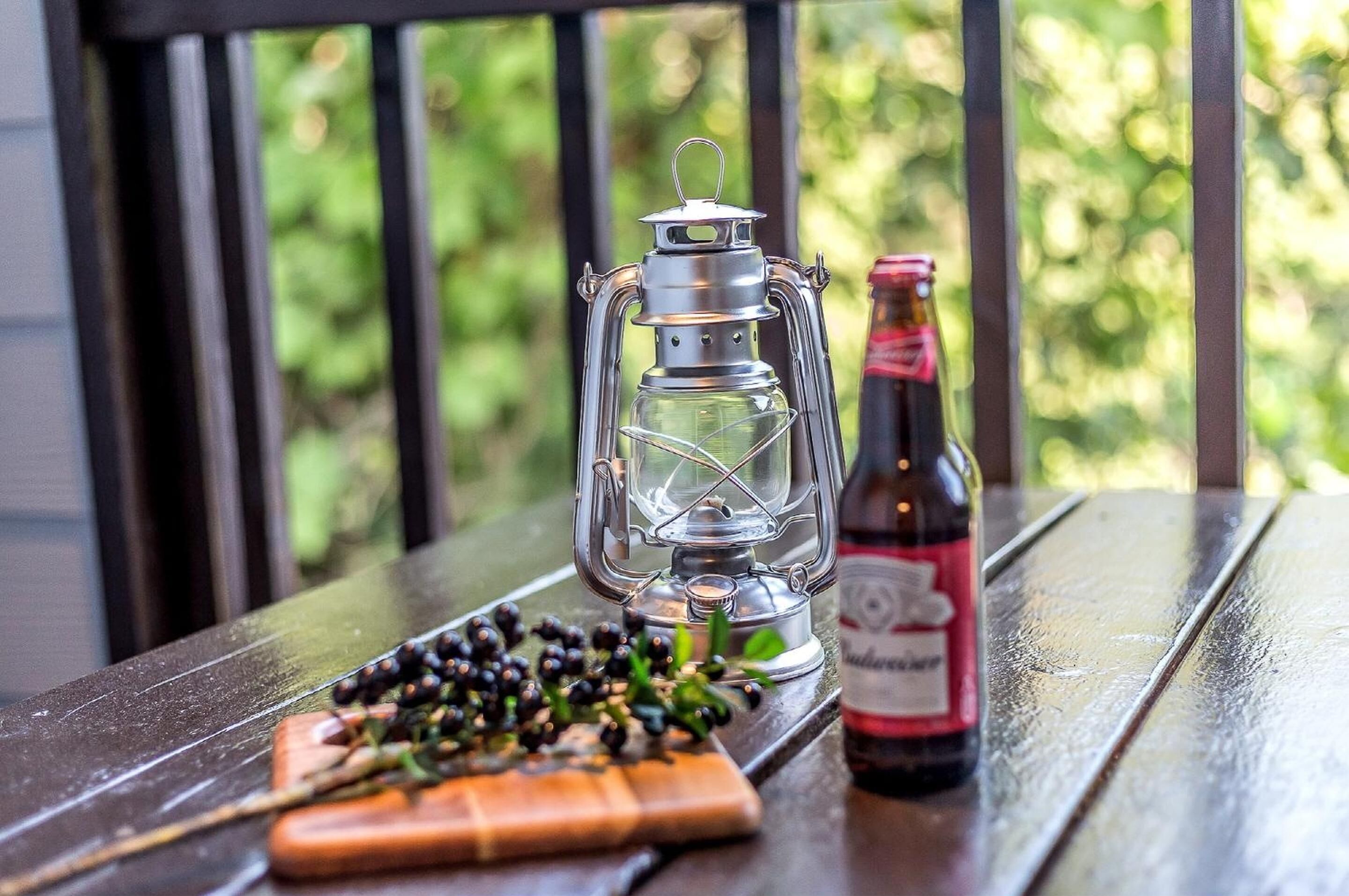 Ein Laternenlicht, eine Flasche und ein Holzbrett mit Beeren auf einem Holztisch.