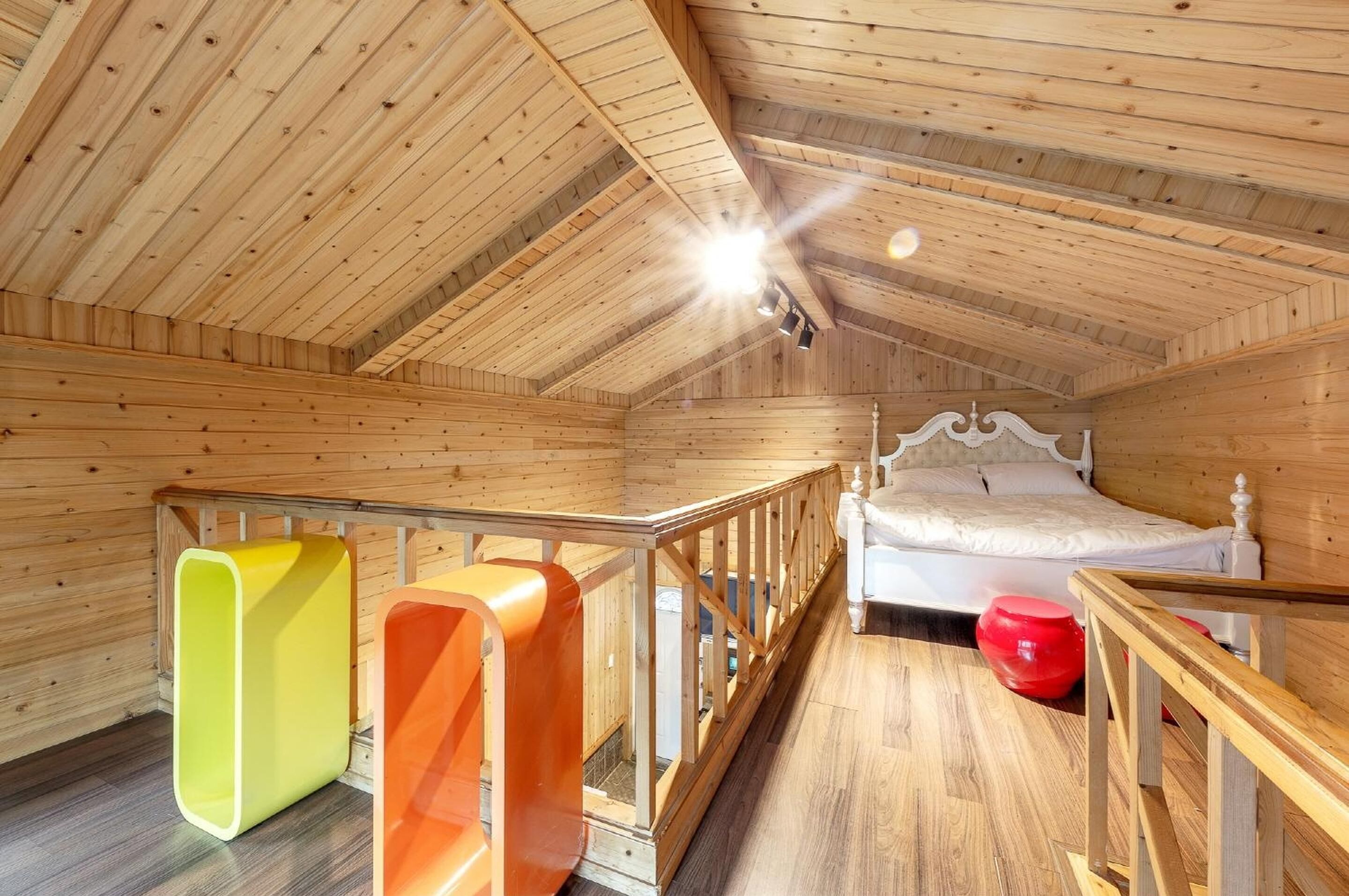 A wooden room with a bed, a staircase, and two colorful chairs.