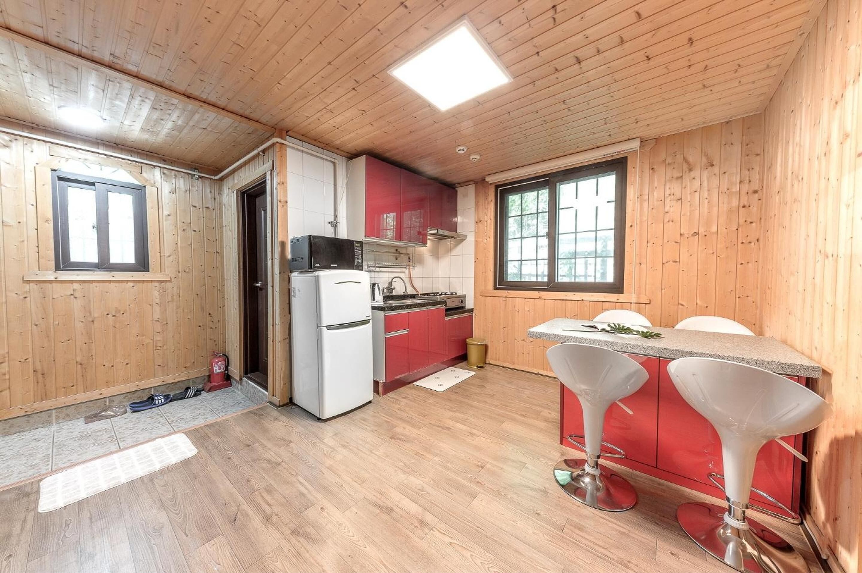 A compact kitchen with wooden walls, a refrigerator, a microwave, red cabinets, and a window.