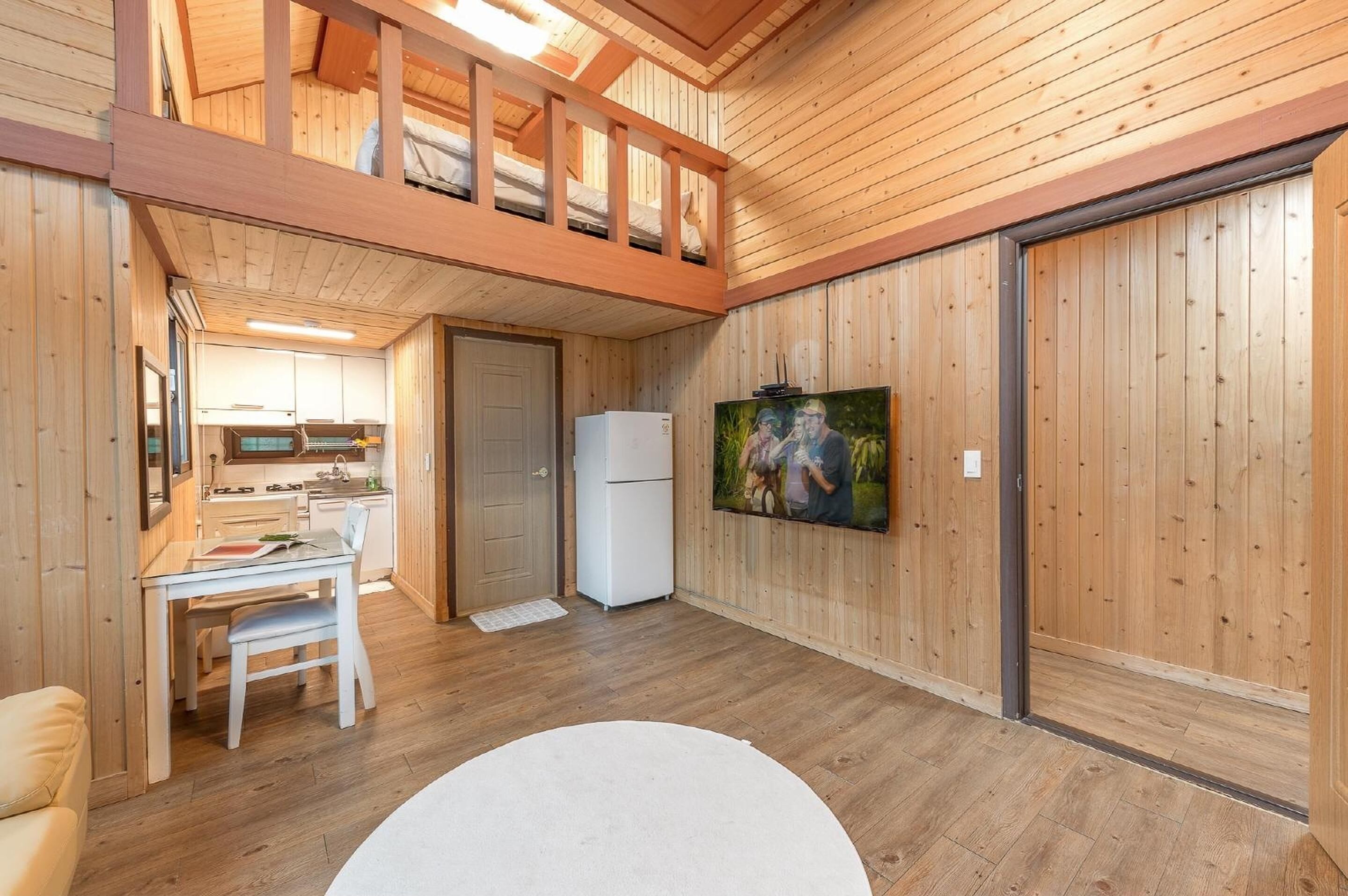 Un interior de madera con zona de comedor, cocina y un televisor en la pared.