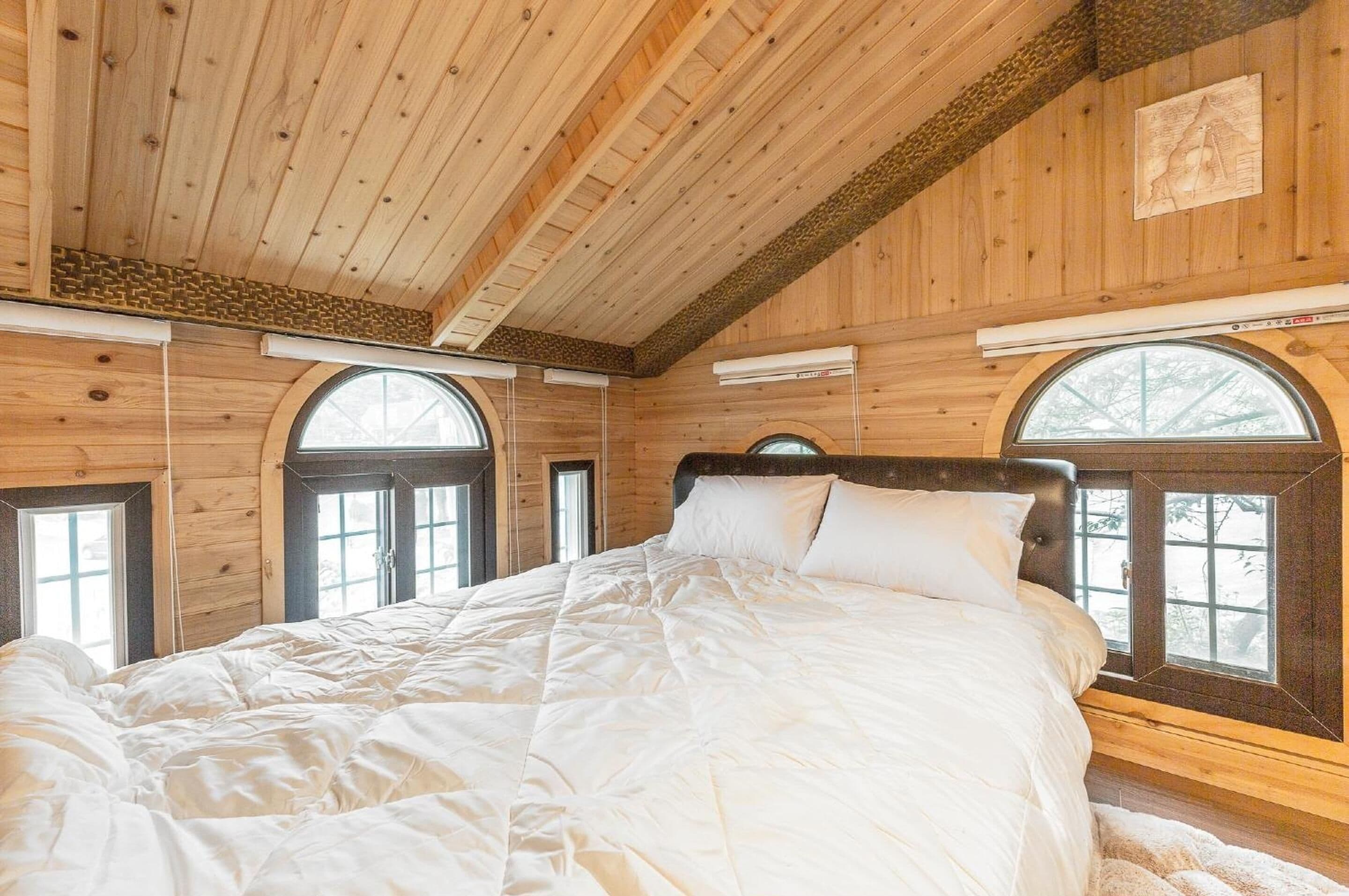 Un dormitorio tipo cabaña de madera con una cama grande, paredes de madera y ventanas de arco.