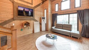 Ein gemütliches Holzhaus-Interieur mit einer Couch, einem an der Wand befestigten Fernseher und einem großen Fenster.