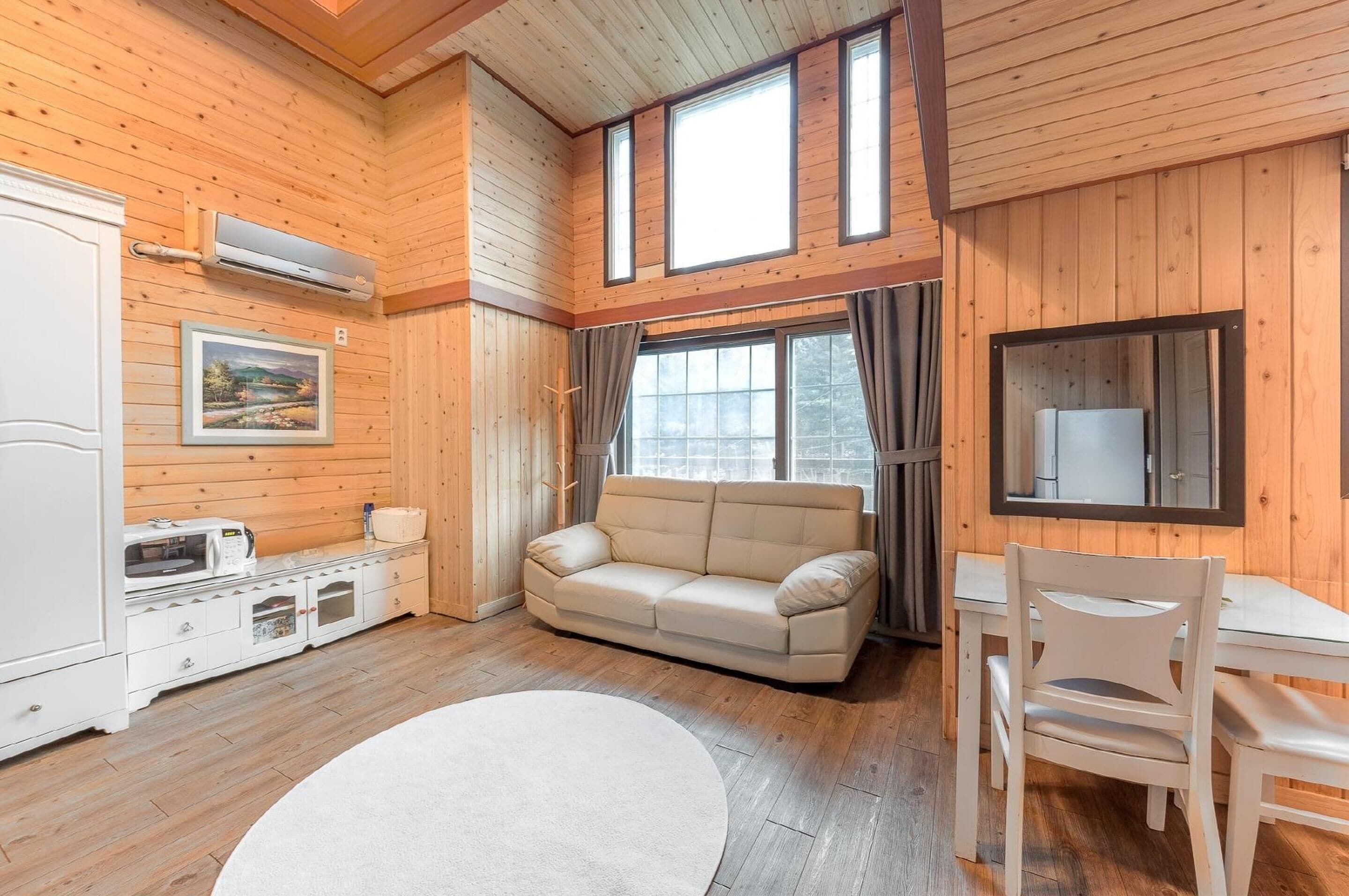 A cozy room with a sofa, a dining table with chairs, a microwave, and a refrigerator.