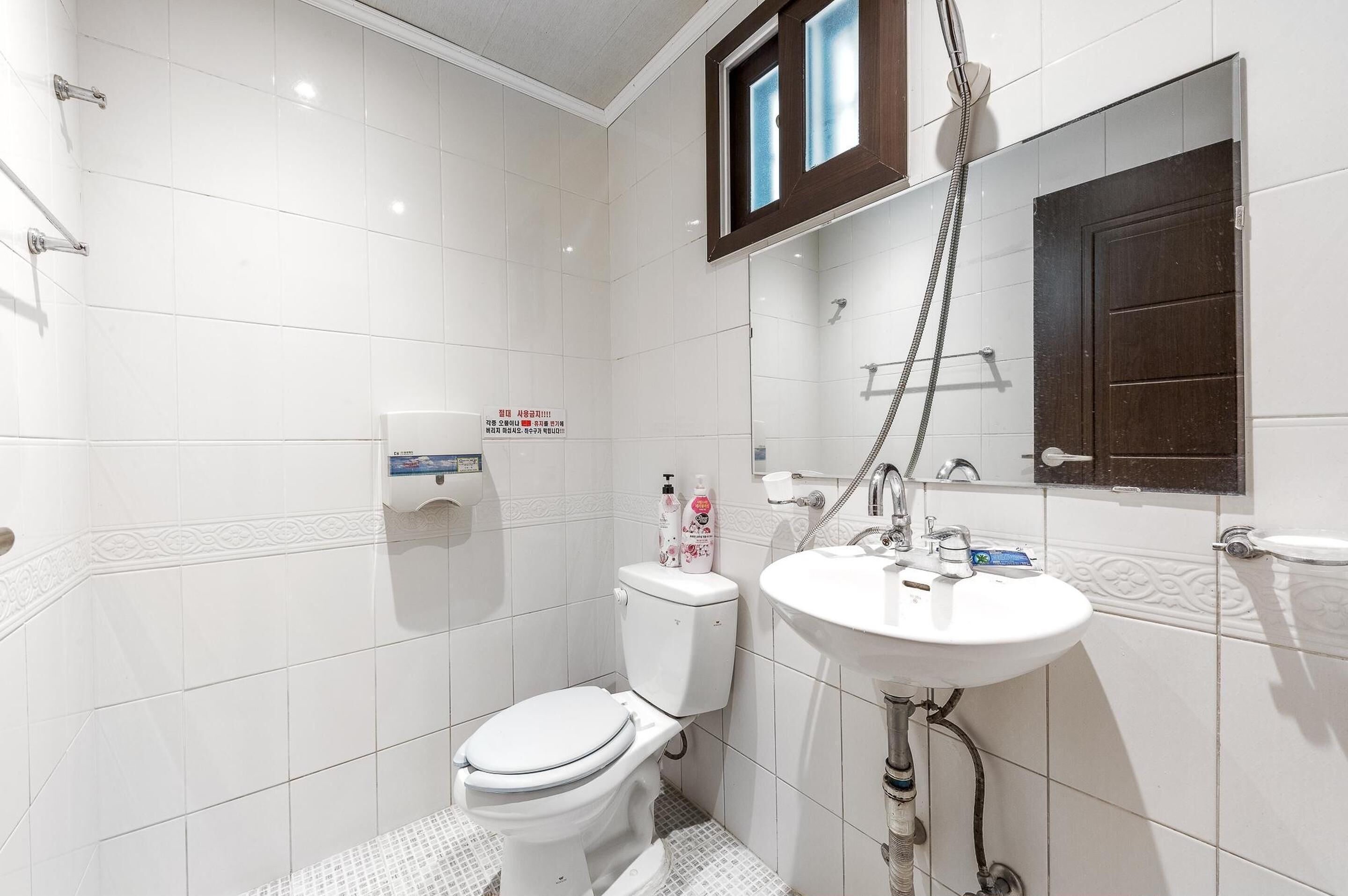 A small, modern bathroom with white tiles, a toilet, a sink, and a shower.