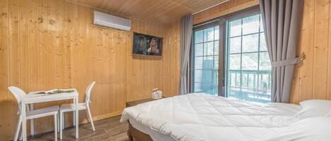 Habitación con paneles de madera, una cama, una mesa con sillas y un ventanal con cortinas.