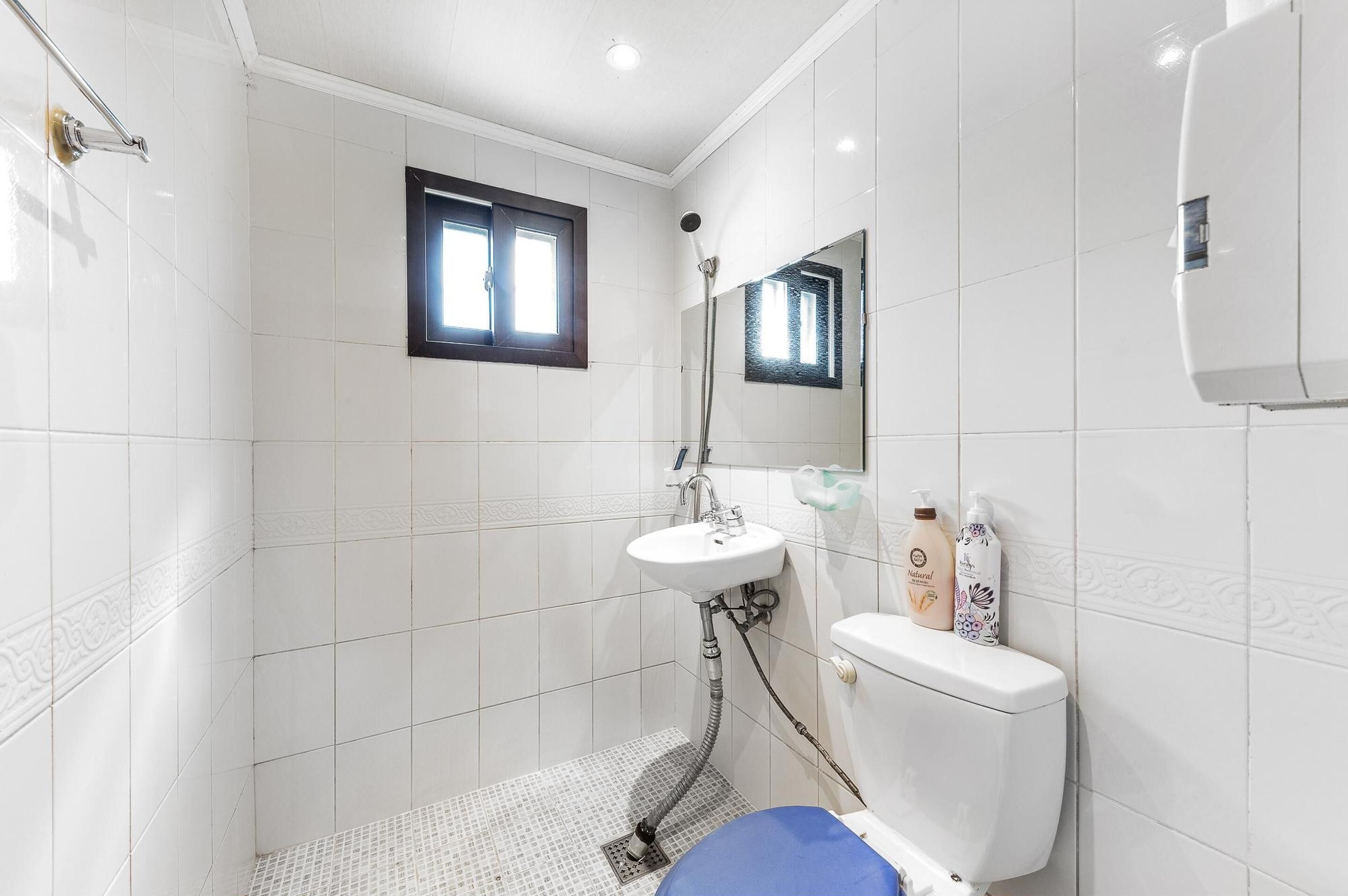 Un baño con azulejos blancos, un lavamanos, un inodoro y una ducha.