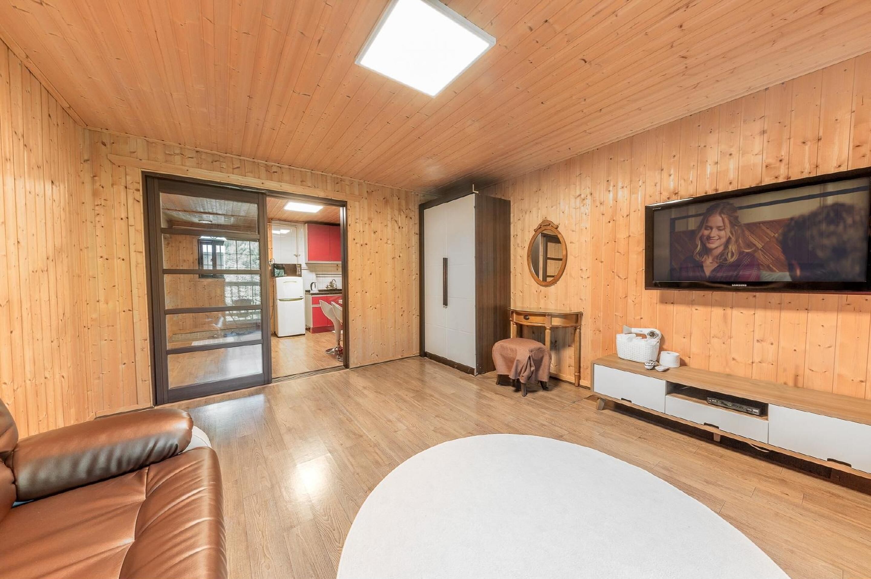 Una habitación con paneles de madera, un sofá de cuero, una mesa redonda blanca, un televisor y un pequeño taburete.