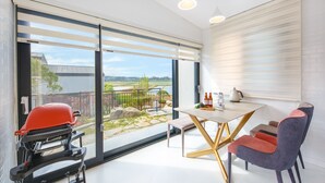 Una habitación moderna con un gran ventanal corredera que da a un balcón, una mesa con sillas y una butaca roja.