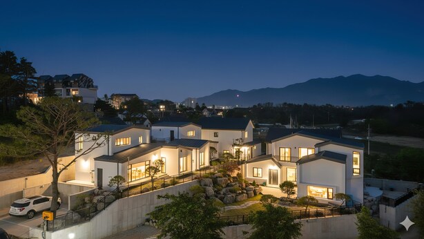 Zona residencial con casas modernas al anochecer, con ventanas bien iluminadas y un jardín ajardinado.
