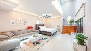 Una sala de estar moderna y bien iluminada con un sofá, una cama, una mesita de centro y una escalera que sube a un nivel superior.