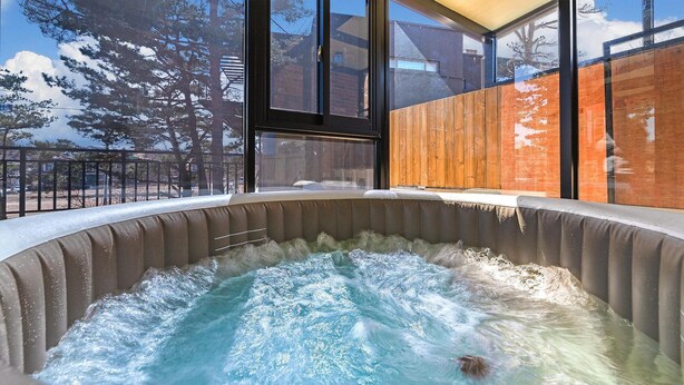 A hot tub with a view of trees and buildings through large windows. - Goseong Pinetree Pension (Goseong)
