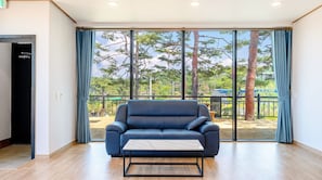 A room with a blue sofa, a small table, and a large window with curtains. - Goseong Pinetree Pension (Goseong)