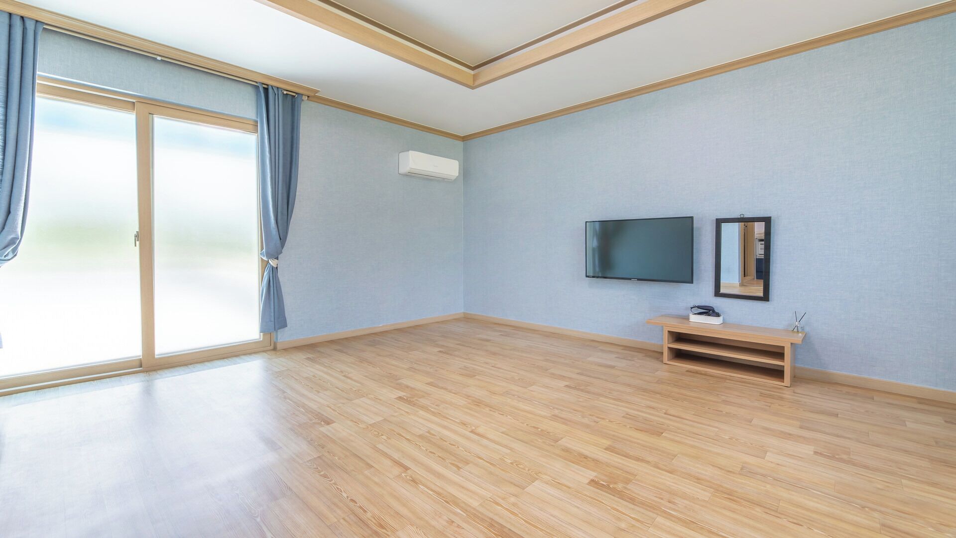 Una habitación con un amplio ventanal corredero, un televisor de pantalla plana, un espejo y un banco de madera.