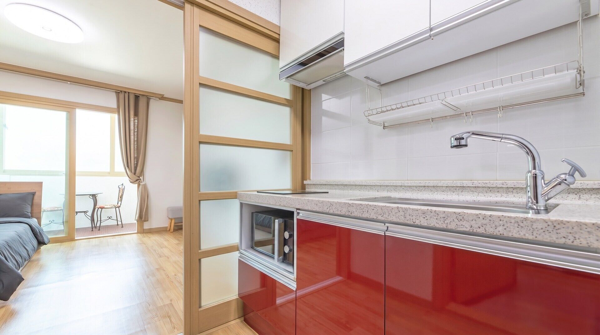 Una cocina moderna con horno integrado, un lavamanos de acero inoxidable y ventana con vistas a un balcón.