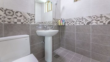 A bathroom with a white pedestal sink, a toilet, and a shower area.