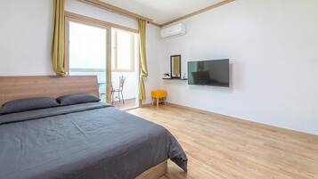 Un dormitorio con una cama, televisión, una silla y un taburete pequeño.