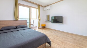 A bedroom with a bed, a television, a chair, and a small stool.