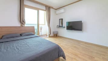 A bedroom with a bed, a television, an air conditioning unit, and a view of the outdoors.