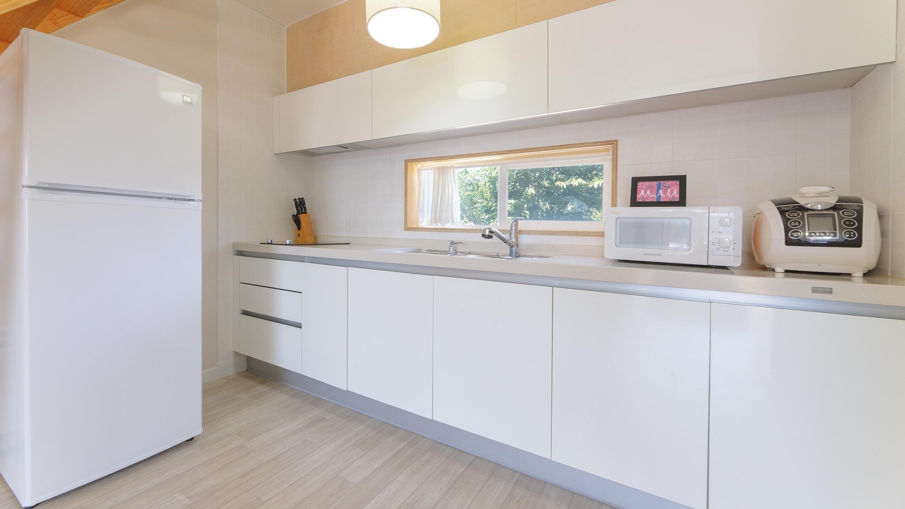A modern kitchen with white cabinets, a built-in microwave, a coffee maker, and a window above the sink.