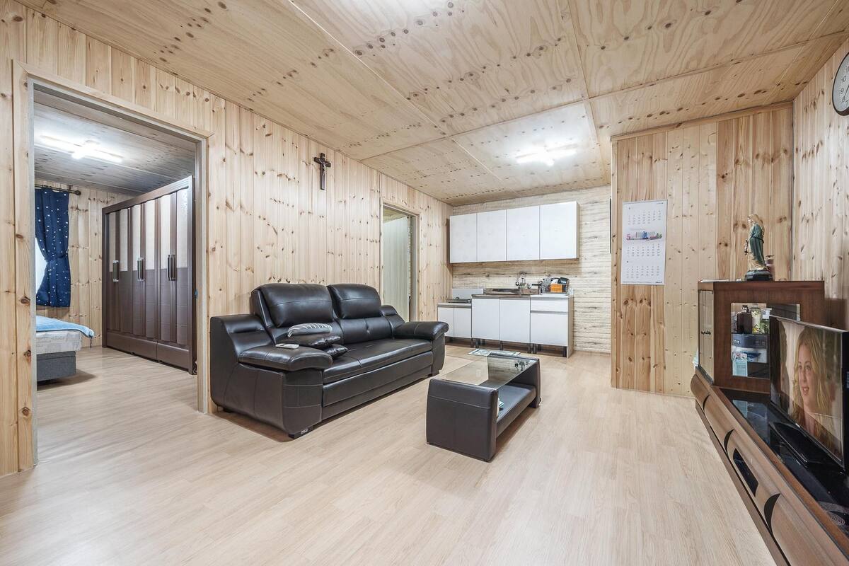 Uma sala de estar com painéis de madeira, um sofá de couro preto, uma mesa de centro de vidro e uma televisão.