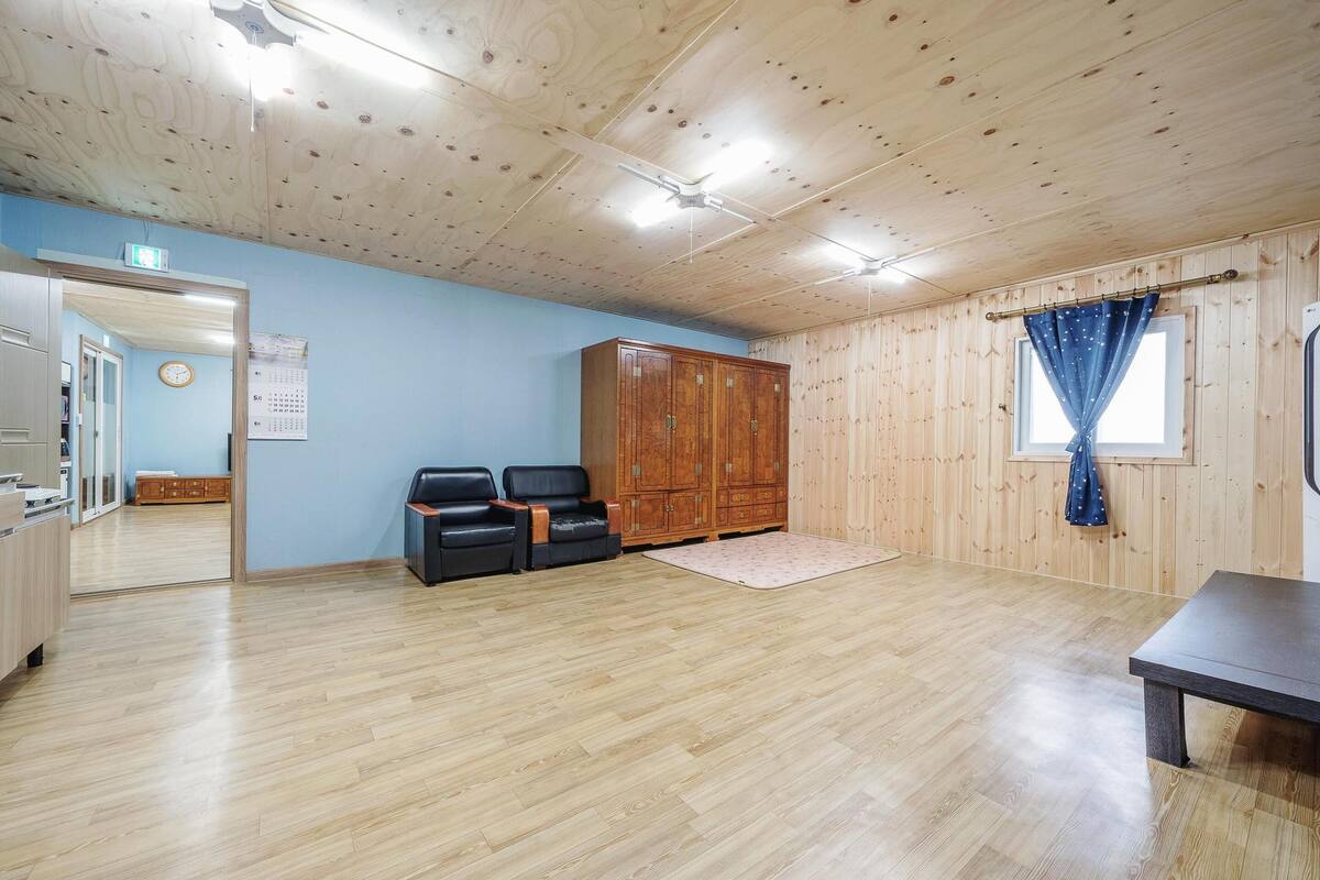 Quarto com piso de madeira, teto de madeira, guarda-roupa de madeira, uma escrivaninha e uma janela com cortinas.