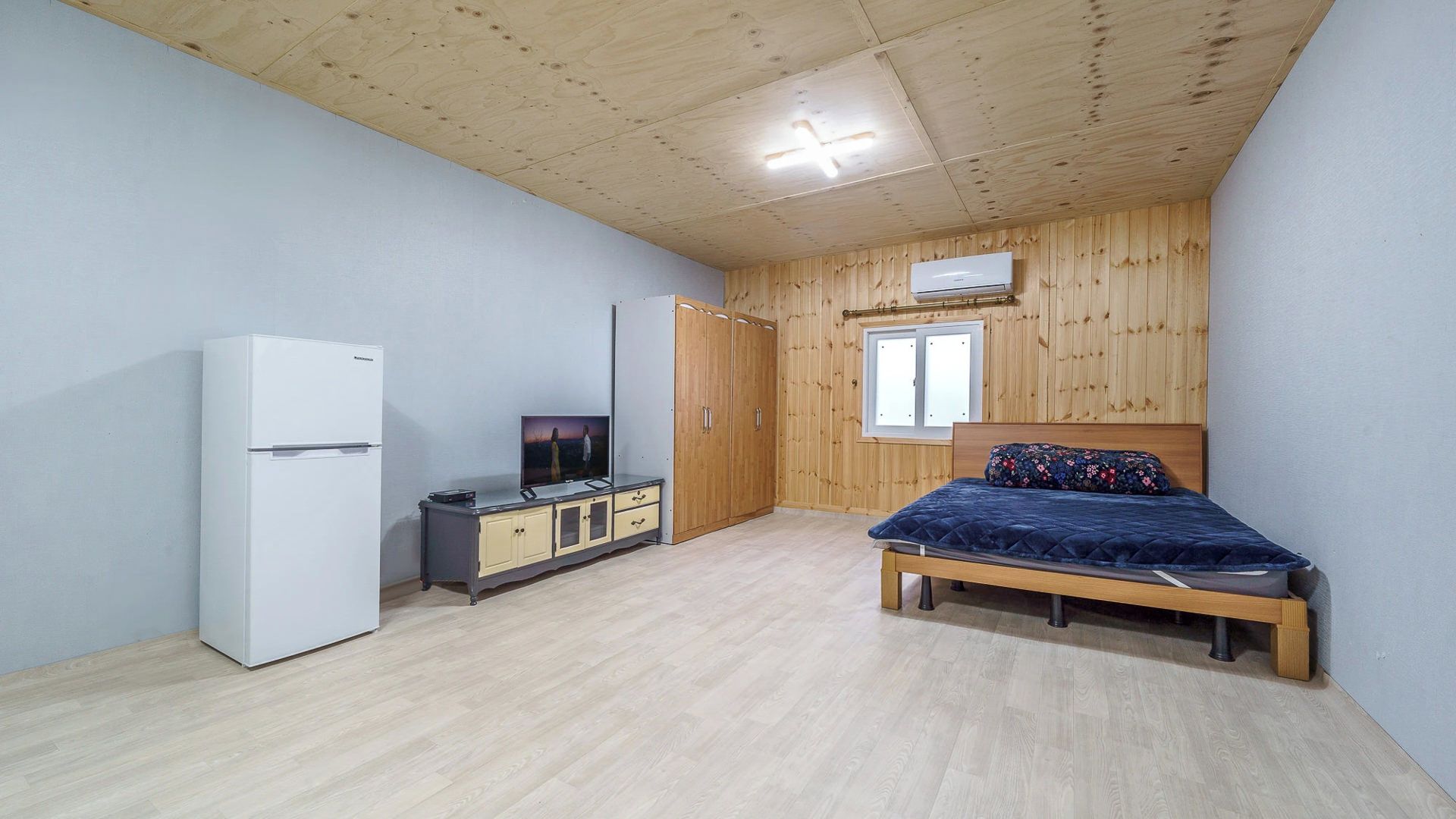 Una camera da letto con un letto, un armadio, una televisione e un frigorifero.