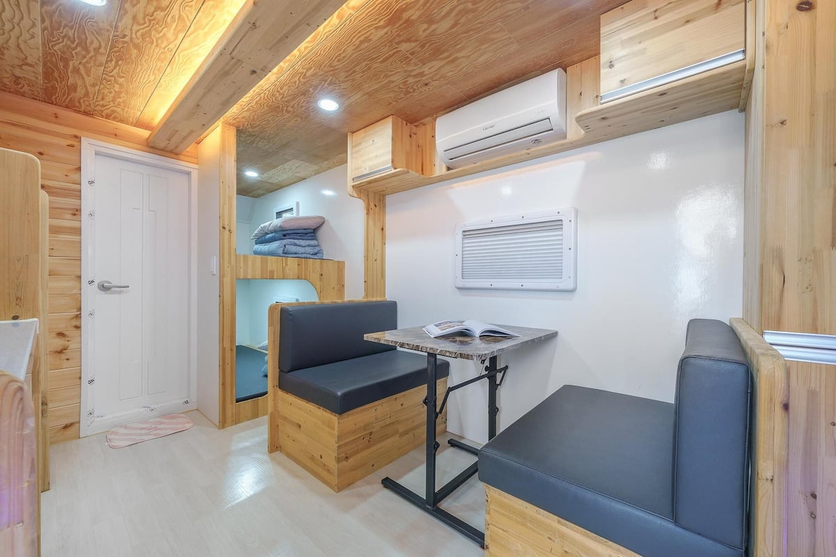 Interior acolhedor de uma cabana, com paredes de madeira, um banco, uma mesa e uma beliche.