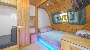 A cozy cabin-style room with a bed, a bench, a small table, and a TV mounted on the wall. - Goseong Jjun Camping Pension (Goseong)