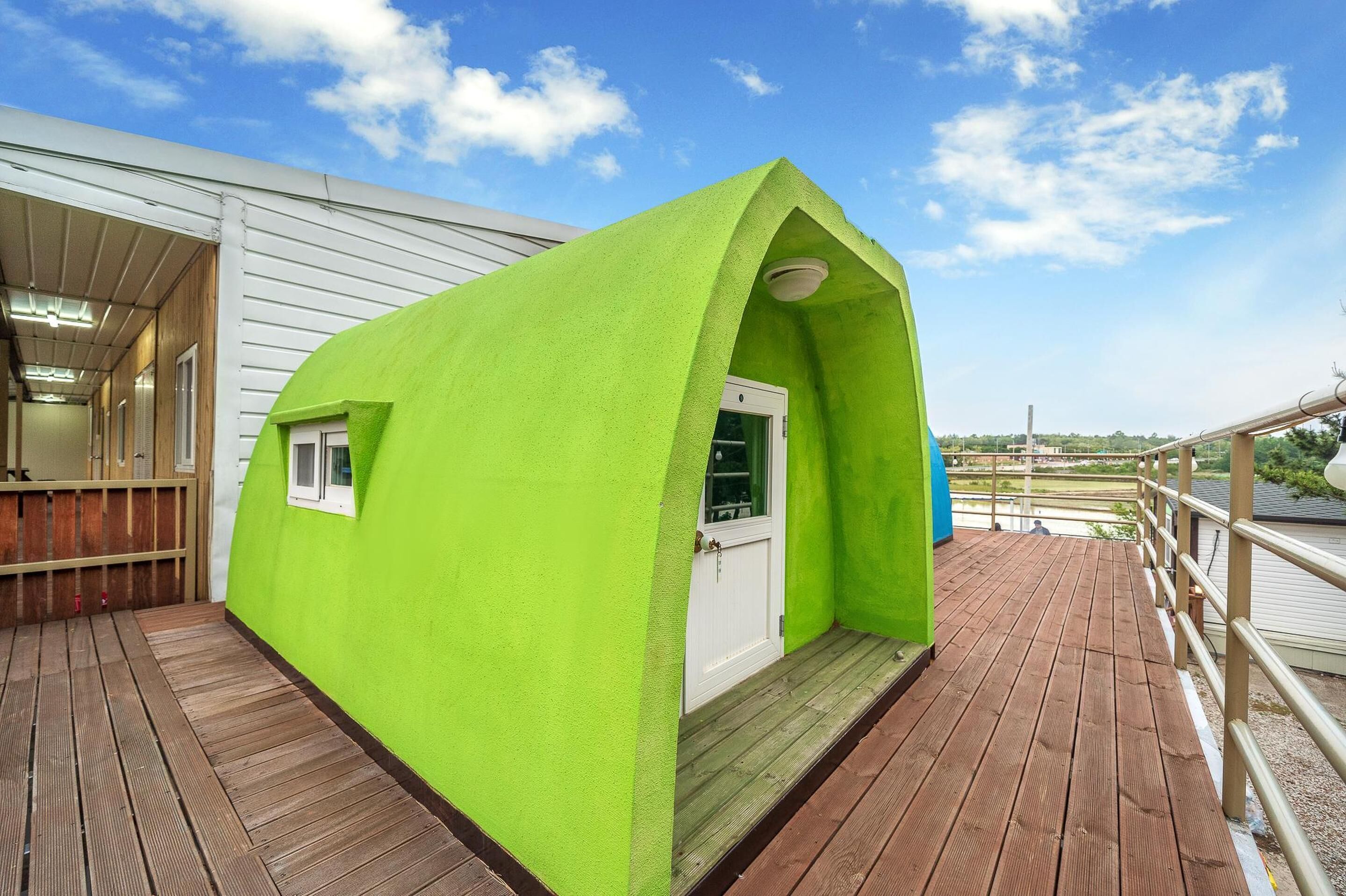 A bright green structure with a door and windows, situated on a wooden deck with a railing.