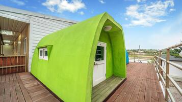 A bright green structure with a door and windows, situated on a wooden deck with a railing.