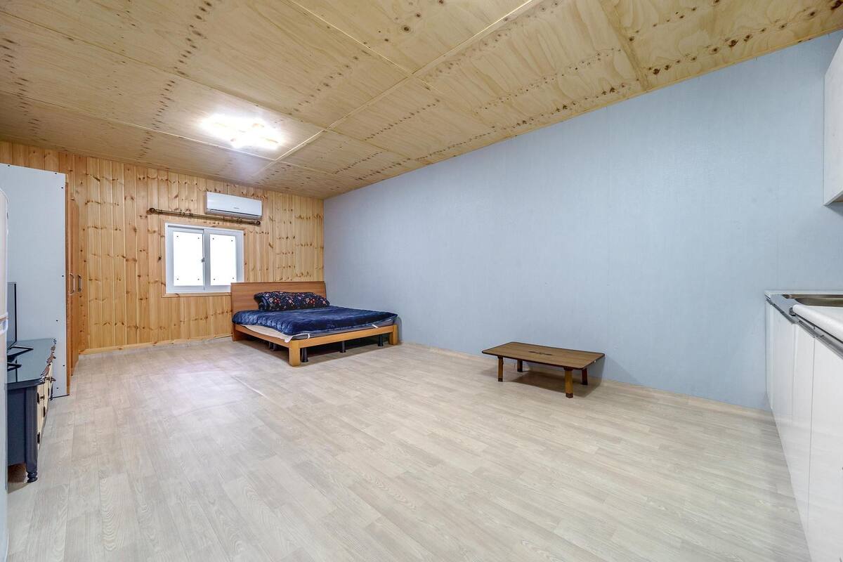 Quarto com paredes de madeira, uma cama, uma mesinha e uma janela.
