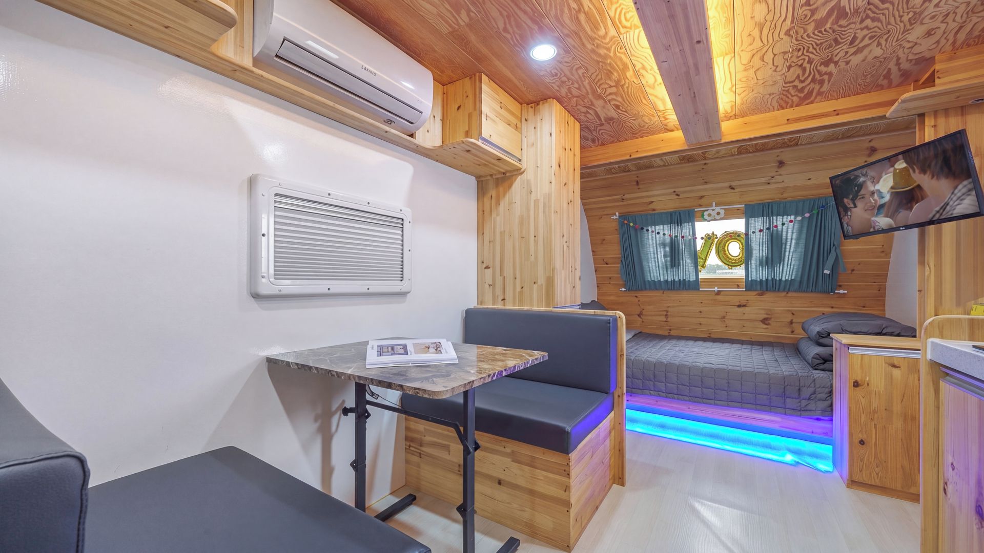 Una habitación compacta con cama, una mesita, un sofá, un equipo de aire acondicionado y un televisor.