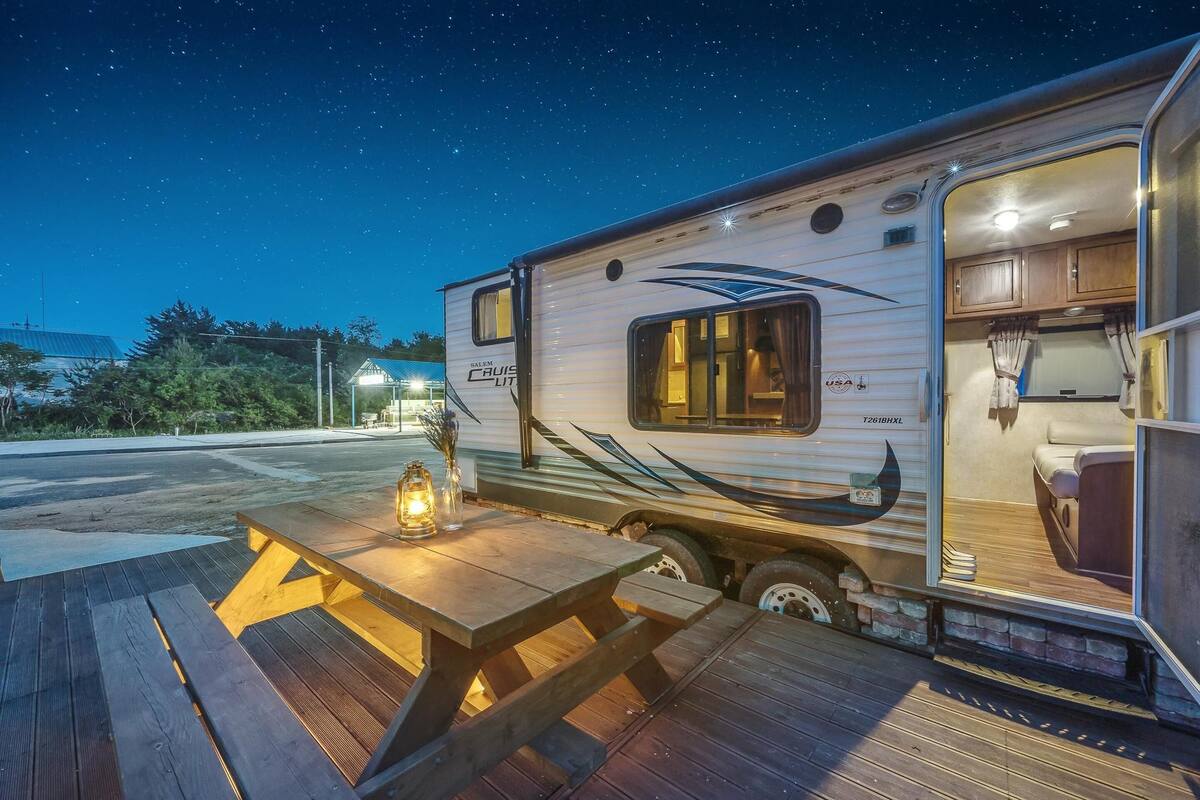 Uma motorhome bem iluminada com área de refeições, céu estrelado e vista da paisagem ao redor.