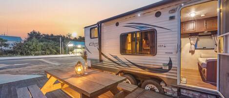 A recreational vehicle with a kitchen area, a dining table with a lantern, and a view of a building in the background.