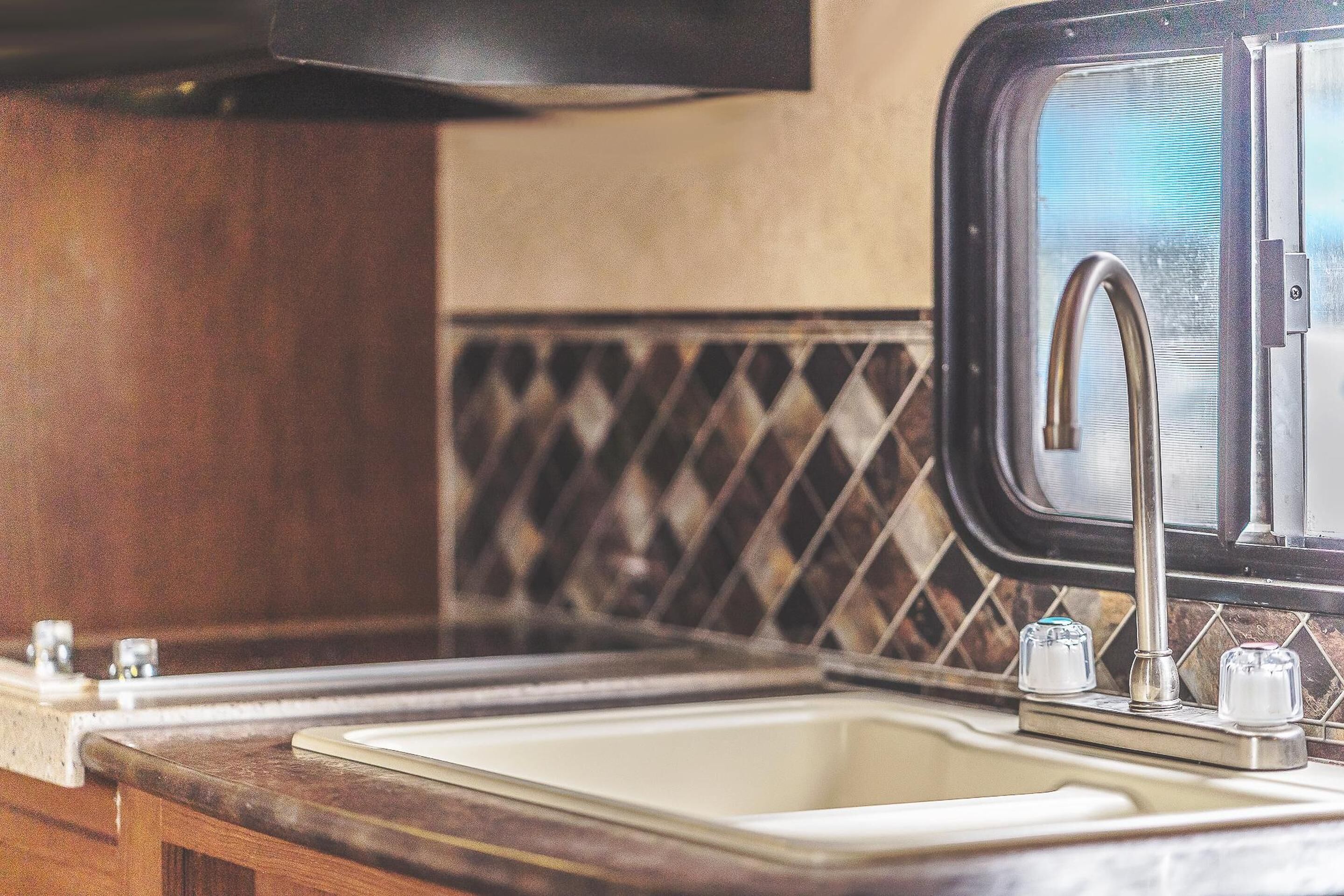 Una cocina con un lavamanos, grifo y ventana.