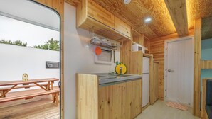 A compact kitchen with wooden cabinets, a countertop, and a small sink. There is a wooden bench and a table outside the door. - Goseong Jjun Camping Pension (Goseong)