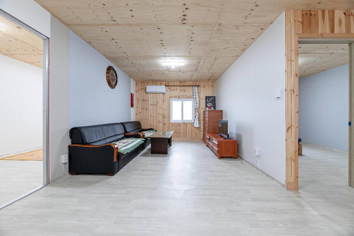 Uma sala de estar moderna com teto de madeira, sofá de couro preto, armário de madeira e uma televisão.