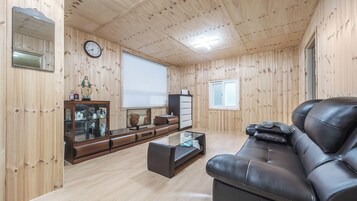 Una habitación con paneles de madera, un sofá de cuero, un televisor, un reloj y una pequeña estatua sobre un mueble.