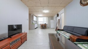 A living room with a television on a wooden cabinet, a sofa with a quilt, and a dining area with a table and chairs. - Goseong Jjun Camping Pension (Goseong)