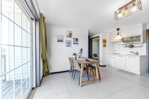 Una cocina moderna con armarios blancos, un comedor con mesa y sillas de madera, y un amplio ventanal con cortinas.