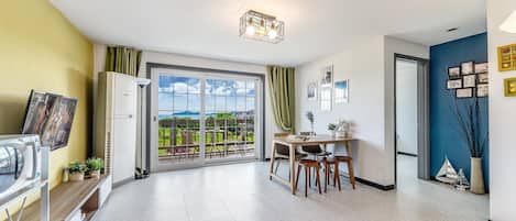 A modern living room with a dining area, a large window with a view, and a ceiling light fixture.