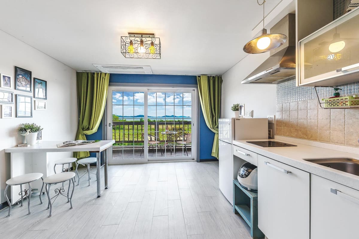 A modern kitchen with a dining area, large windows, and a view of the outdoors.