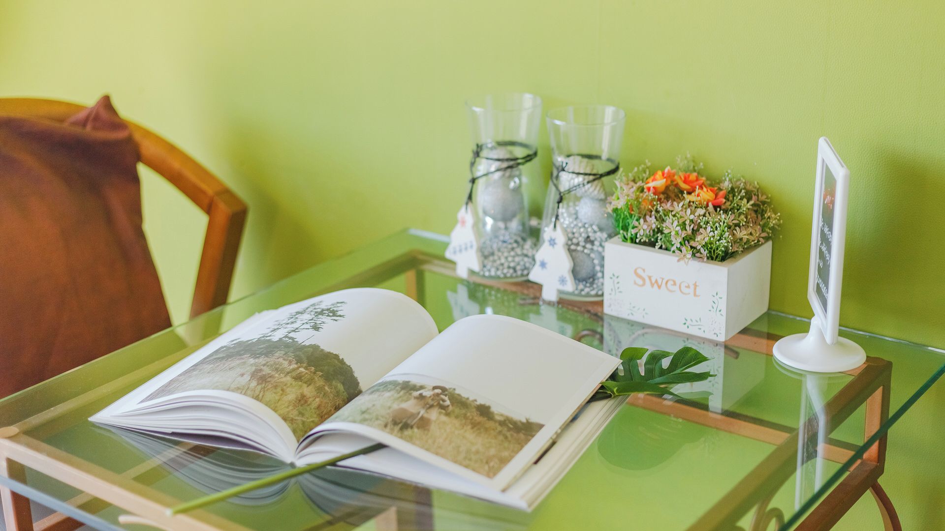Un tavolo con un libro aperto, una piccola pianta in vaso e un cartello con scritto 'Sweet'.