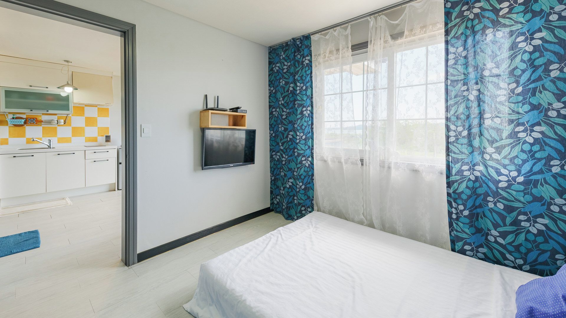 A bedroom with a bed, a television on the wall, and a window with curtains.