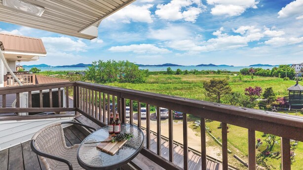 A wooden deck with a table and chairs, overlooking a grassy landscape with a gazebo and distant mountains. - Ganghwa Rodemhouse Pension (Incheon)