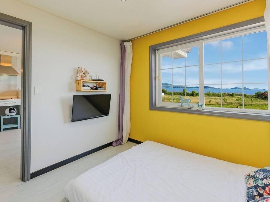 Un dormitorio con cama, televisor montado en la pared y ventana con vista al paisaje.