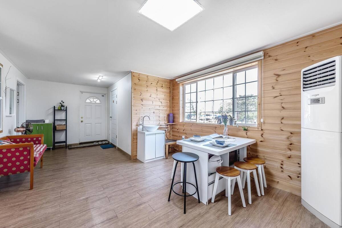 A modern kitchen with a large window, wooden wall paneling, and a dining area with stools.
