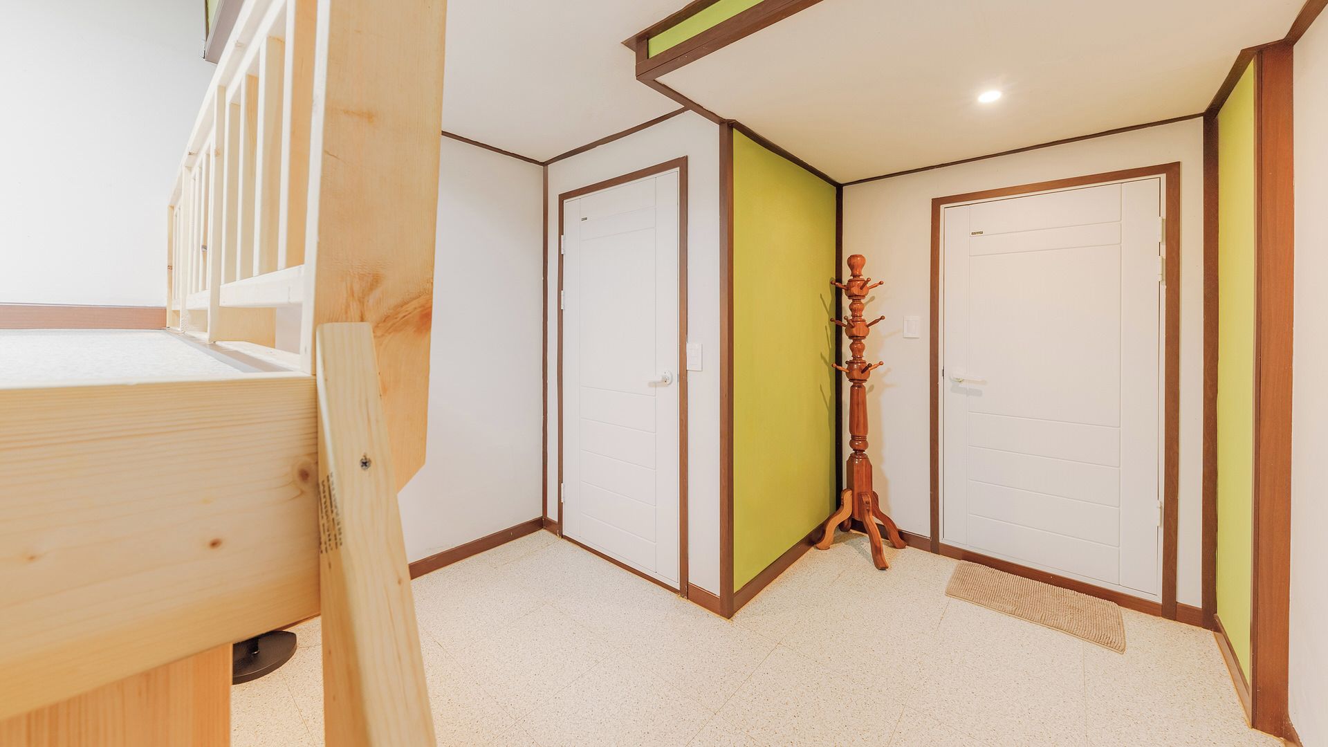 A room with a bunk bed, a wooden coat rack, and two doors, one with a green panel.